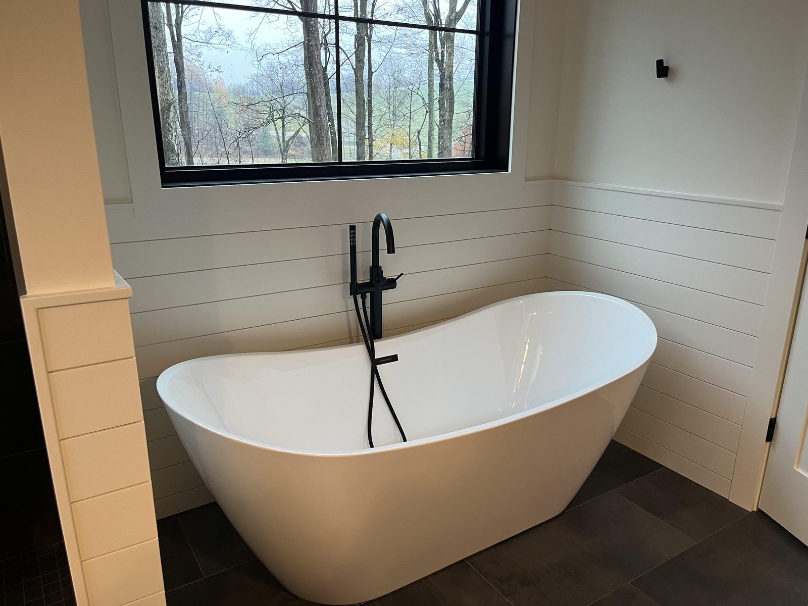 Primary bathroom with freestanding soaker tub and shiplap walls overlooking woods
