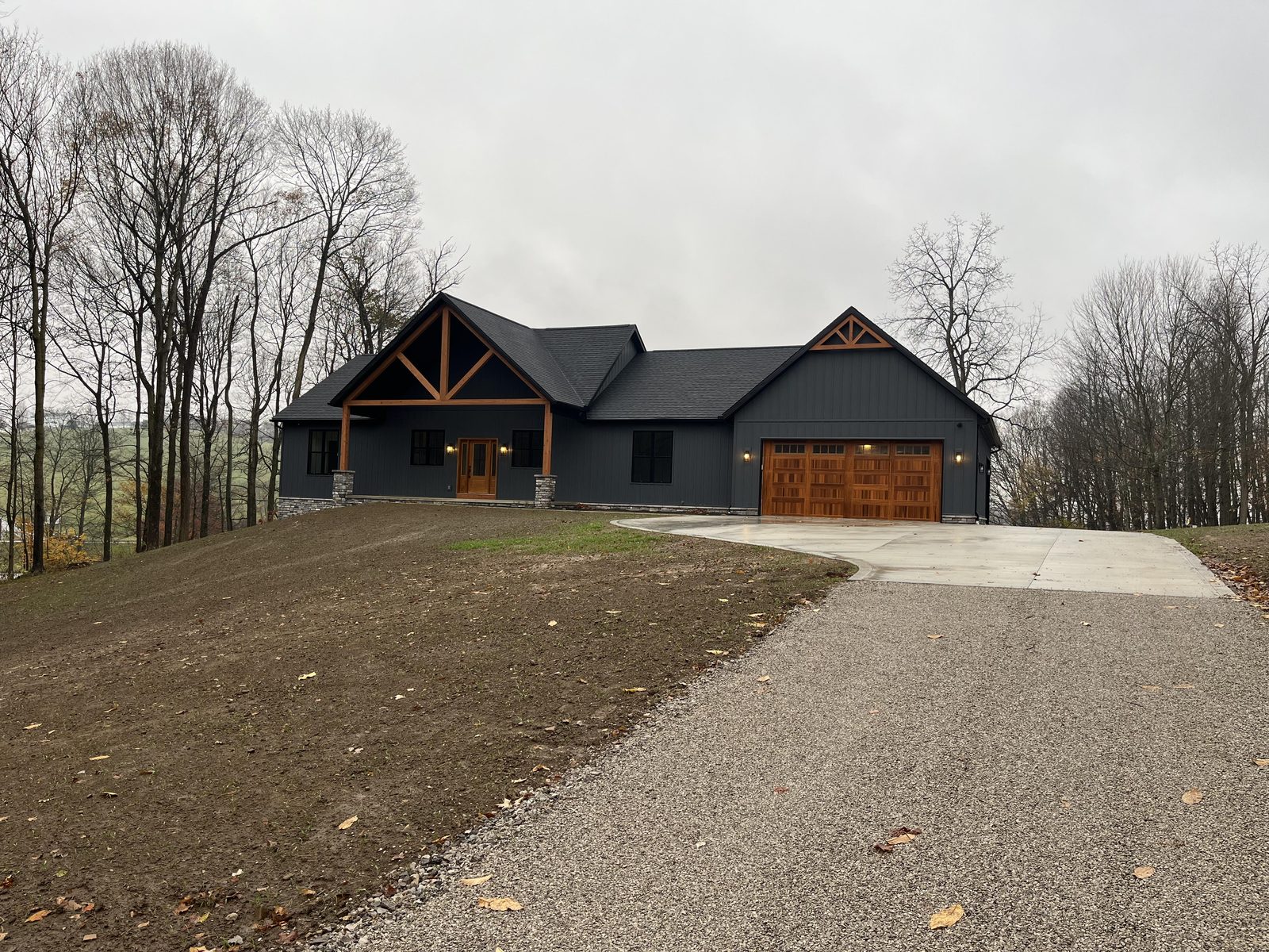 Sorrenti Homes custom charcoal timber-frame home with cedar garage doors on a hillside